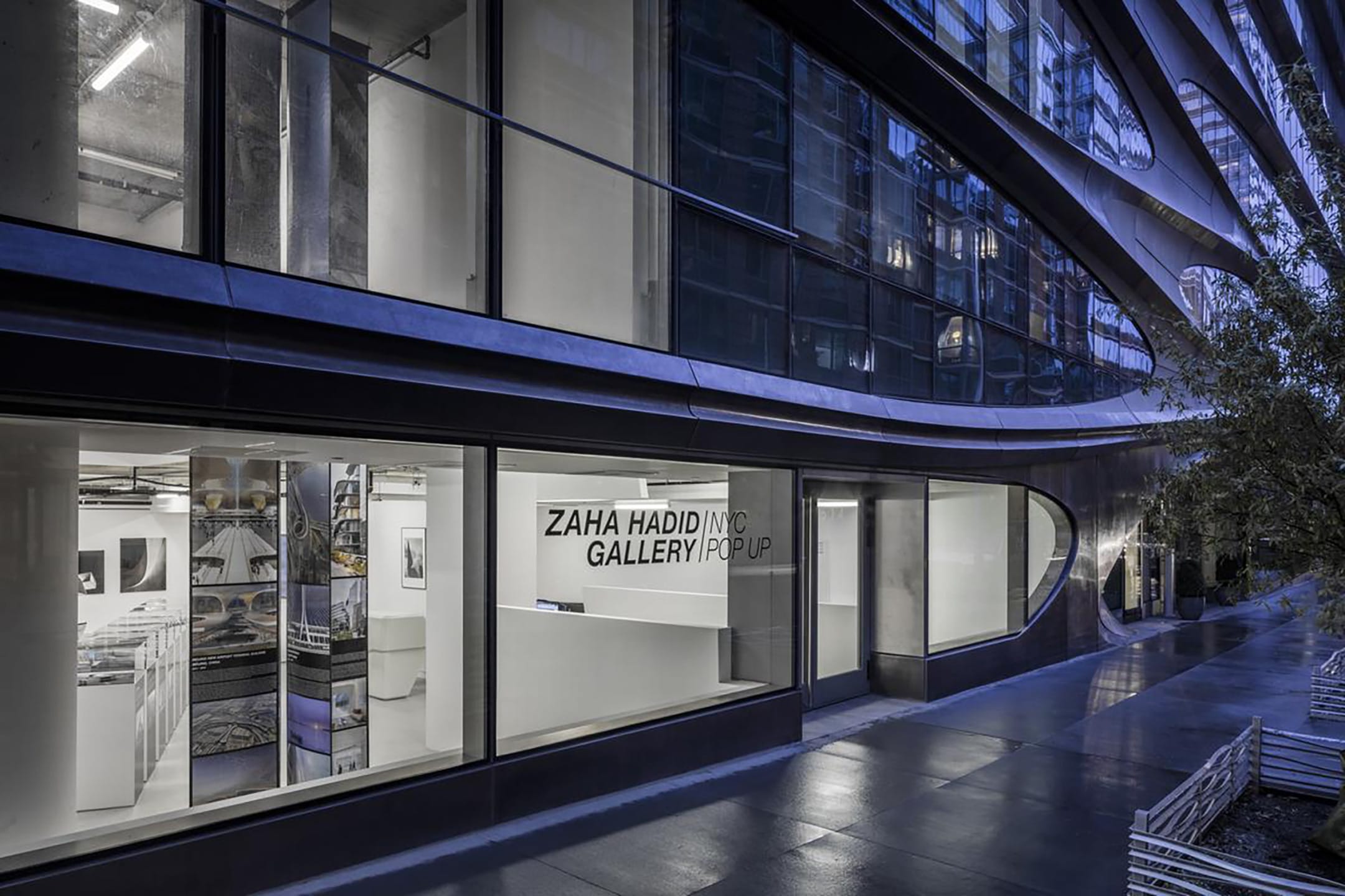 Exterior view of Zaha Hadid Gallery popup with glass windows, modern architecture, and nighttime lighting.