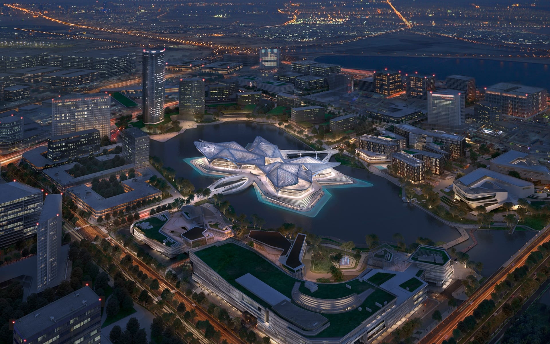 Aerial view of modern architectural complex illuminated at night surrounded by a cityscape with roads and buildings