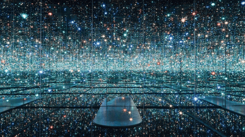 Room with mirrored walls and ceiling reflecting countless small, colorful lights creating an infinite galaxy illusion.