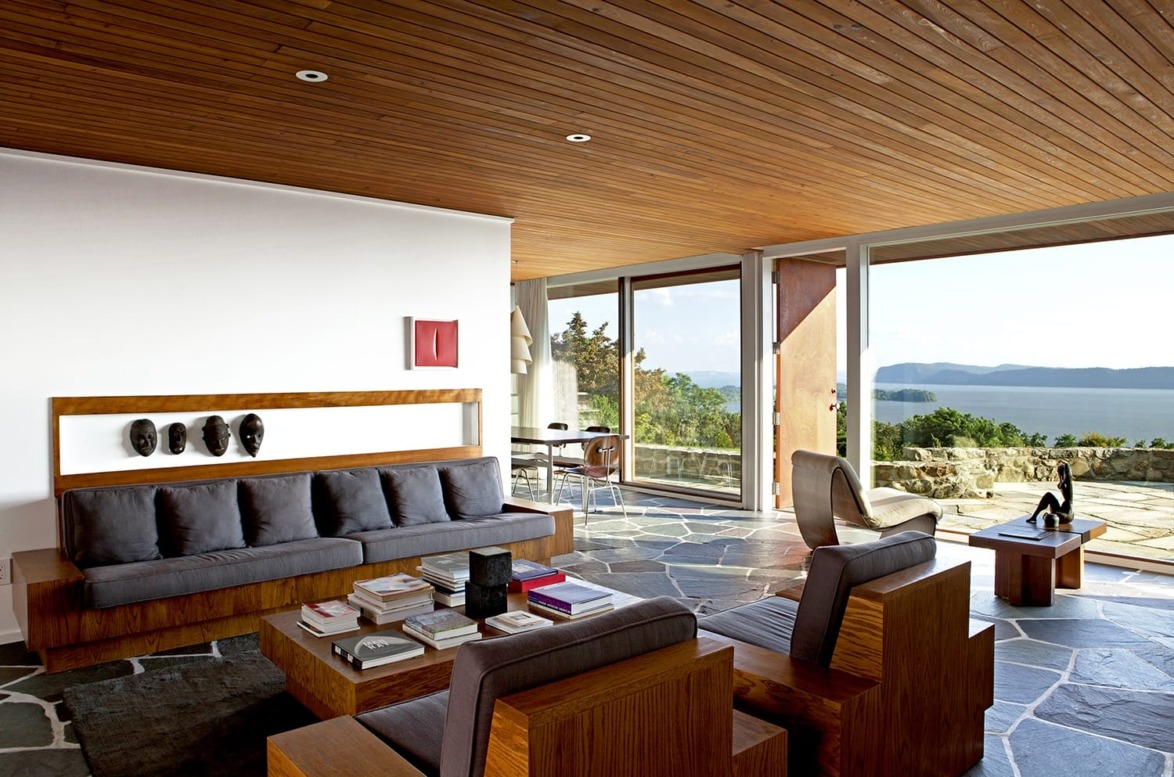 Modern living room with wooden furniture, large windows, and ocean view.