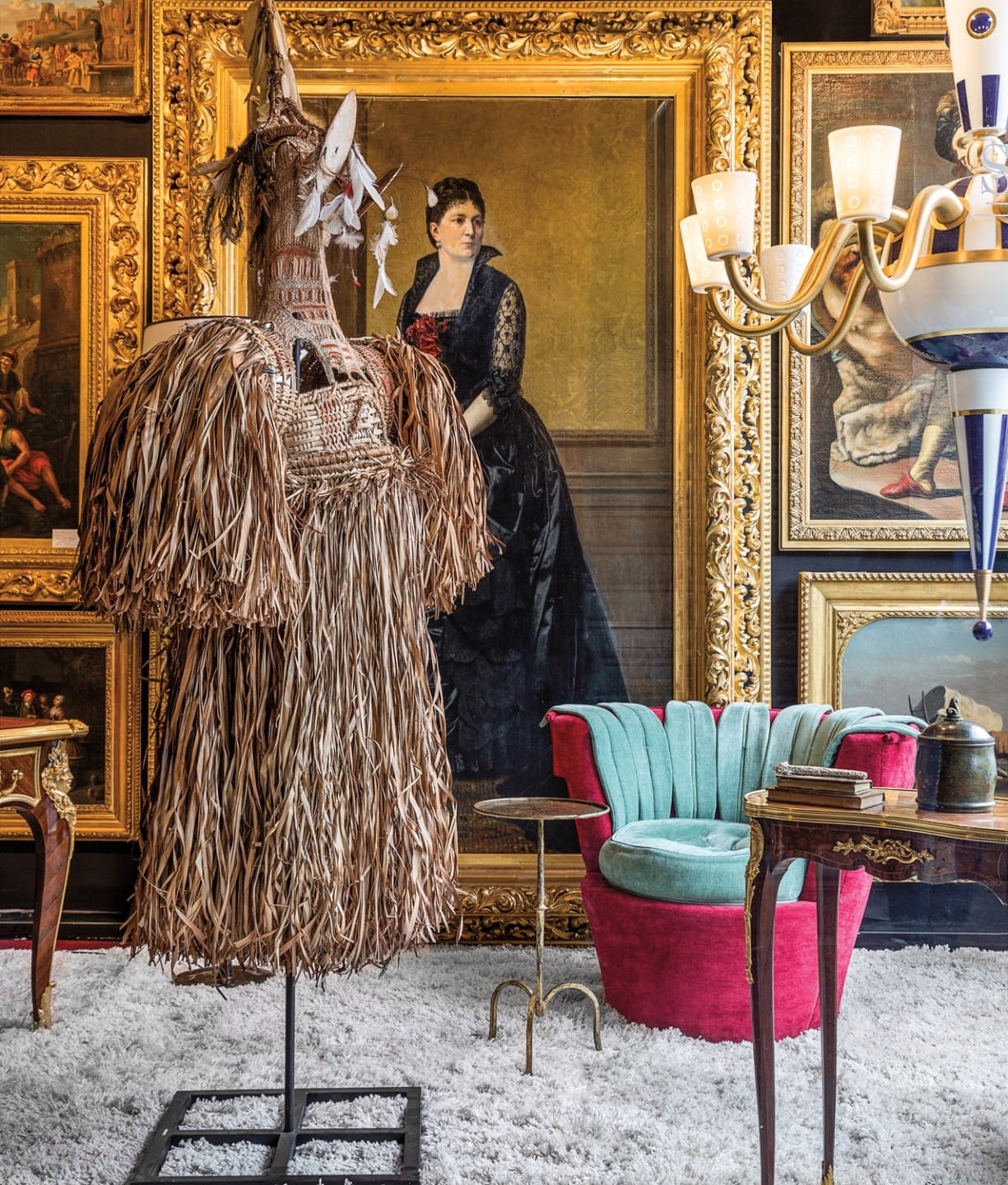 Eclectic room with African sculpture, classical paintings, modern chair, and vintage furniture on a white rug.
