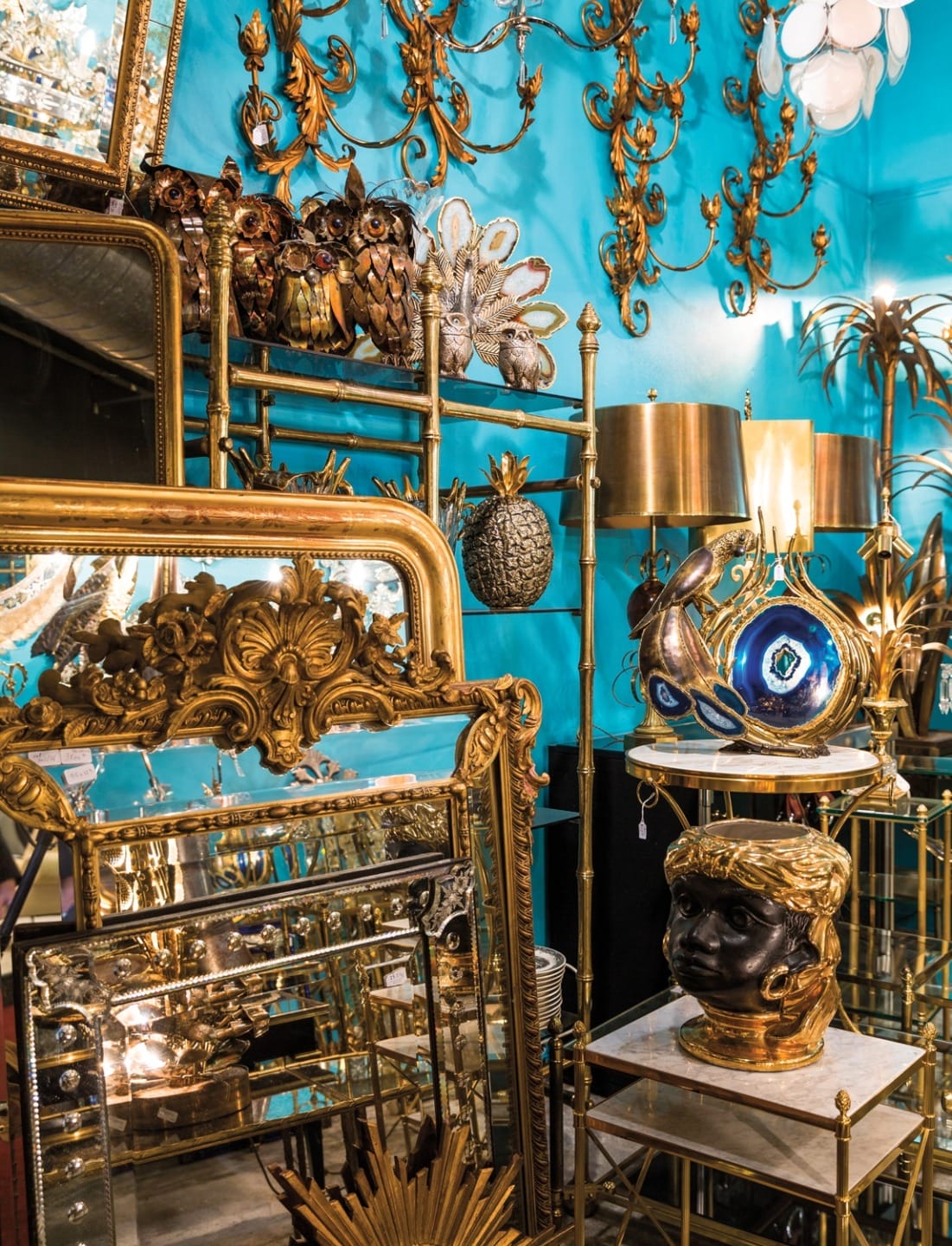 Assortment of vintage mirrors, gilded frames, and brass decor displayed in a vibrant room with turquoise walls.