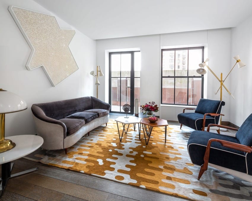 Modern living room with abstract wall art, velvet sofa, blue armchairs, geometric rug, and floor lamps.