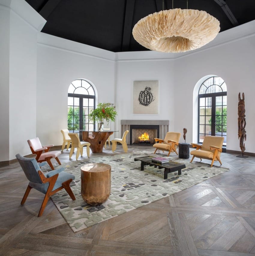 Spacious living room with modern chairs, large chandelier, fireplace, and a mix of natural wood and stone accents.