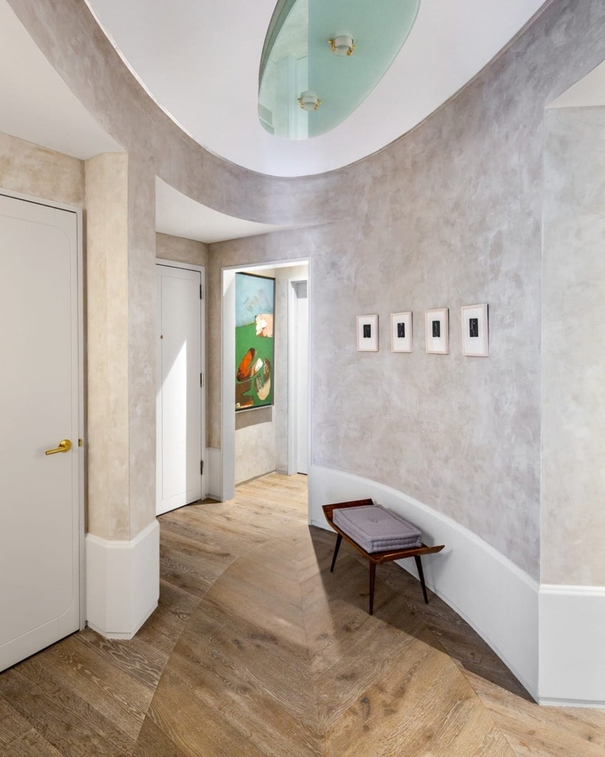 Curved hallway with wooden floor, wall art, bench, and recessed lighting creating a modern interior design ambiance.