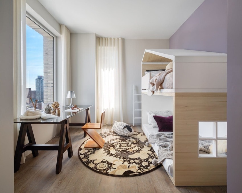 Modern kids' room with bunk bed, stylish desk, round rug, and large window overlooking city skyline.