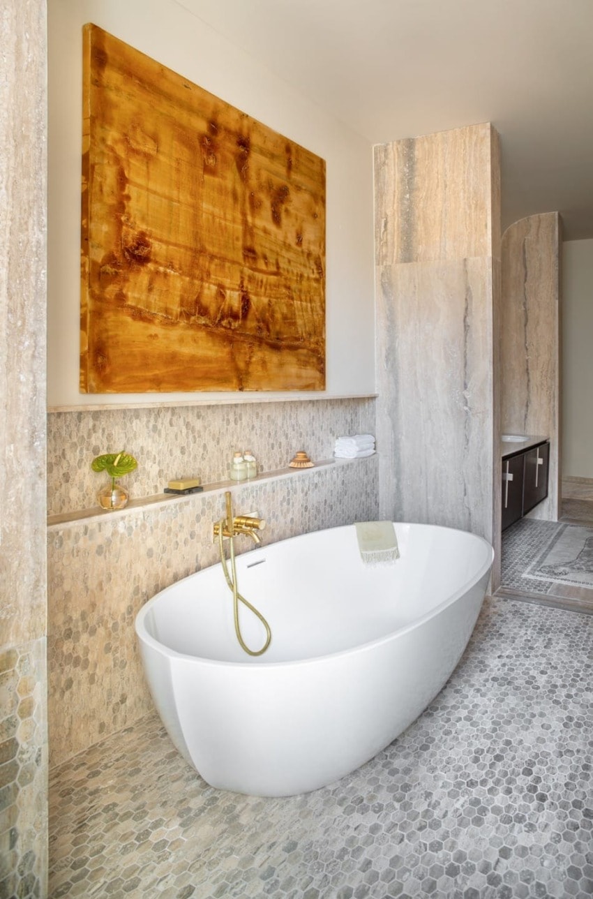 Luxurious modern bathroom with a freestanding white tub, gold fixtures, and elegant stone accents.