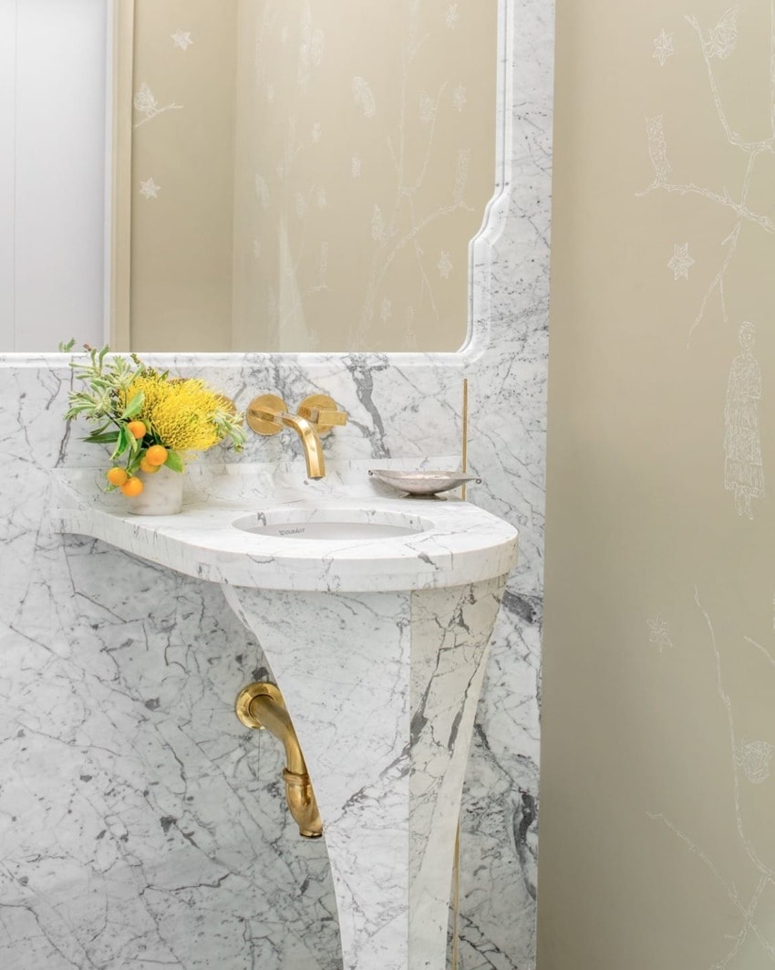 Elegant marble sink with gold fixtures, adorned with a bouquet of yellow flowers and lemons in a luxurious bathroom setting.