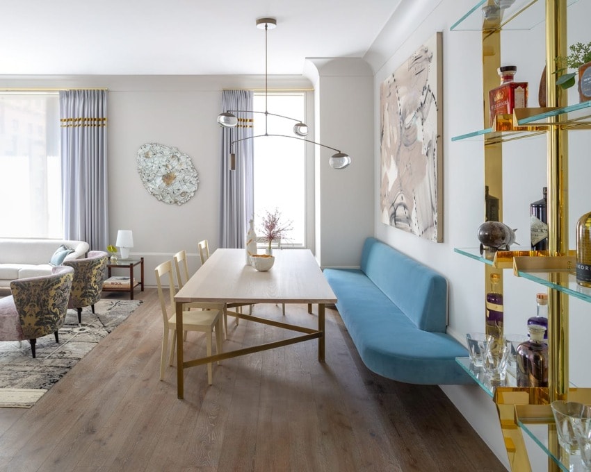 Modern dining room with wooden table, blue cushioned bench, elegant chairs, abstract art, and decorative wall shelves.