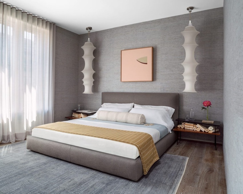 Modern bedroom with gray walls, stylish pendant lights, framed artwork, cozy bed with a plaid throw, and wooden nightstands.