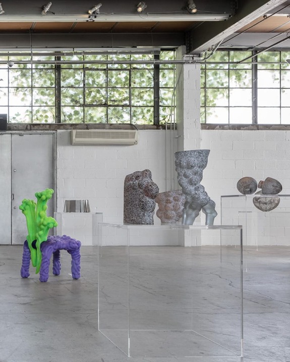 Contemporary art installation featuring abstract sculptures on transparent pedestals in an industrial-style gallery space.