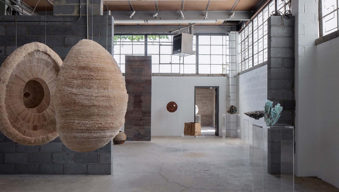 Contemporary art installation in an industrial-style gallery featuring large abstract sculptures and natural light through windows.