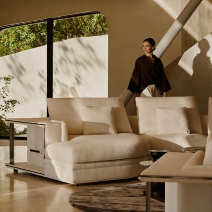 Woman in stylish modern interior with beige sectional sofa and large window, showcasing contemporary home decor design.