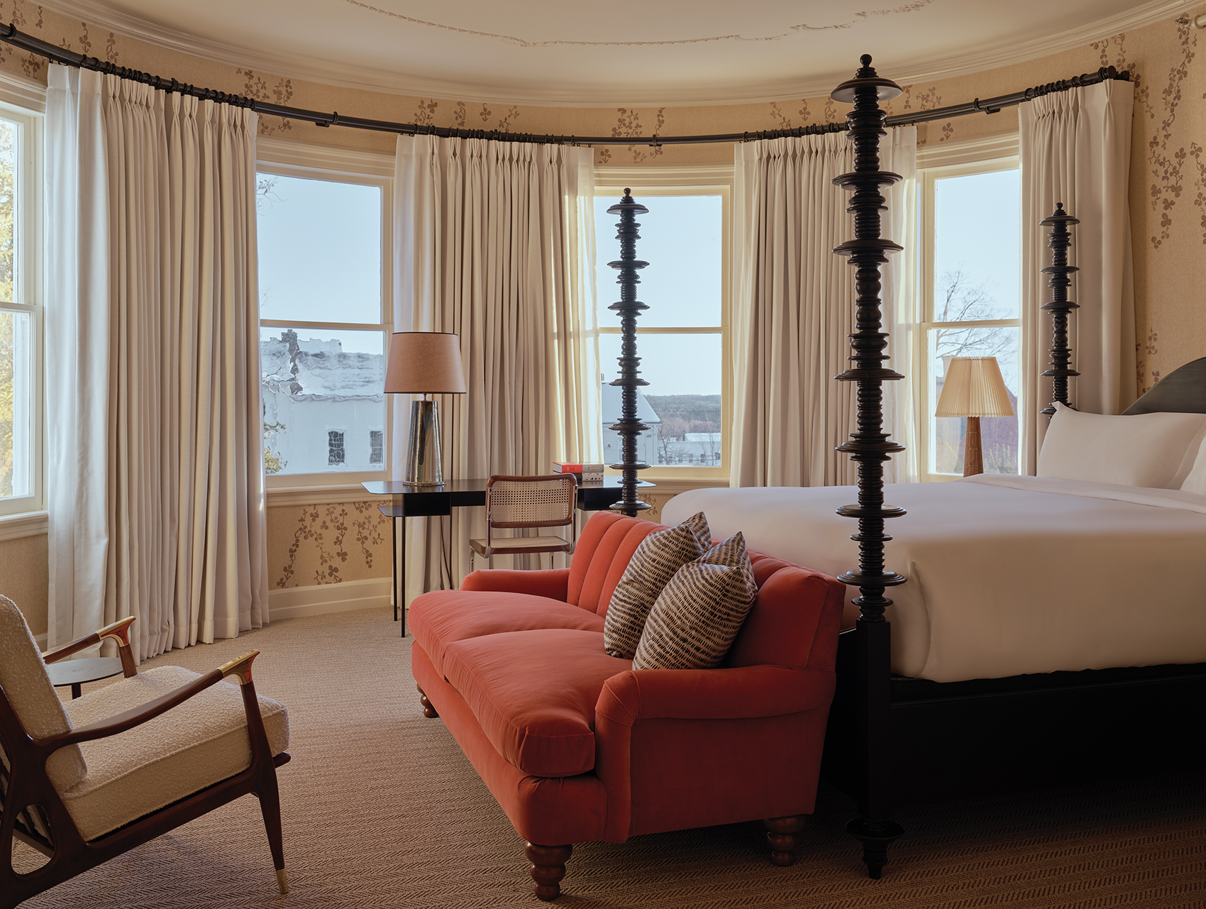 Elegant hotel room with a four-poster bed, red sofa, large windows, and cozy seating area.
