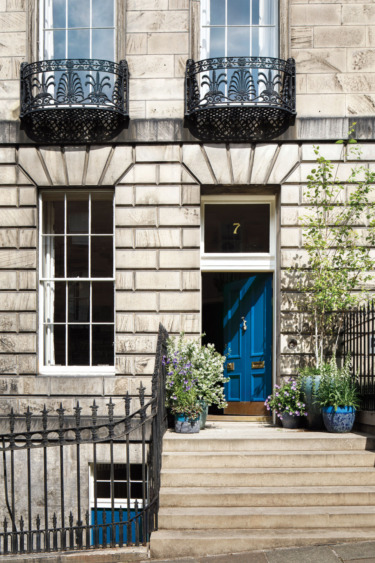 Blue door with number seven on a stone building with potted plants, iron railings, and balcony details.