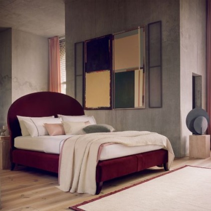 Modern bedroom with a red bed, abstract art on the wall, cozy blankets, and a wooden floor.
