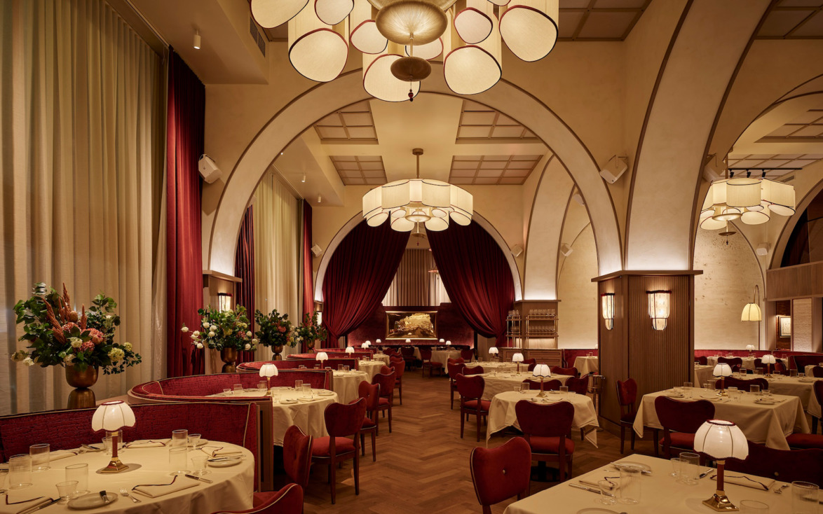 Elegant restaurant interior with archways, red and beige decor, round tables, white tablecloths, and soft ambient lighting.