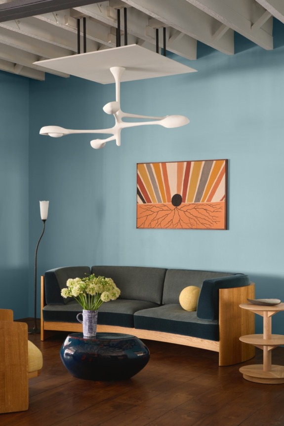 Modern living room with blue walls, abstract art, contemporary furniture, and unique ceiling light fixture.