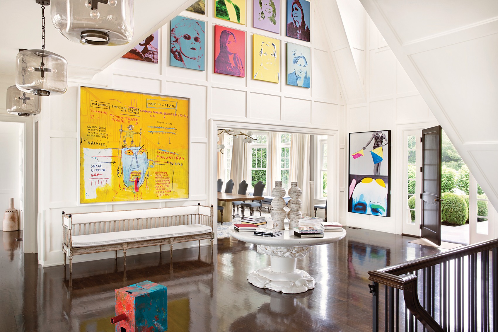 Modern art-filled living room with colorful paintings, white ceiling, dark wooden floor, round table, and natural light.
