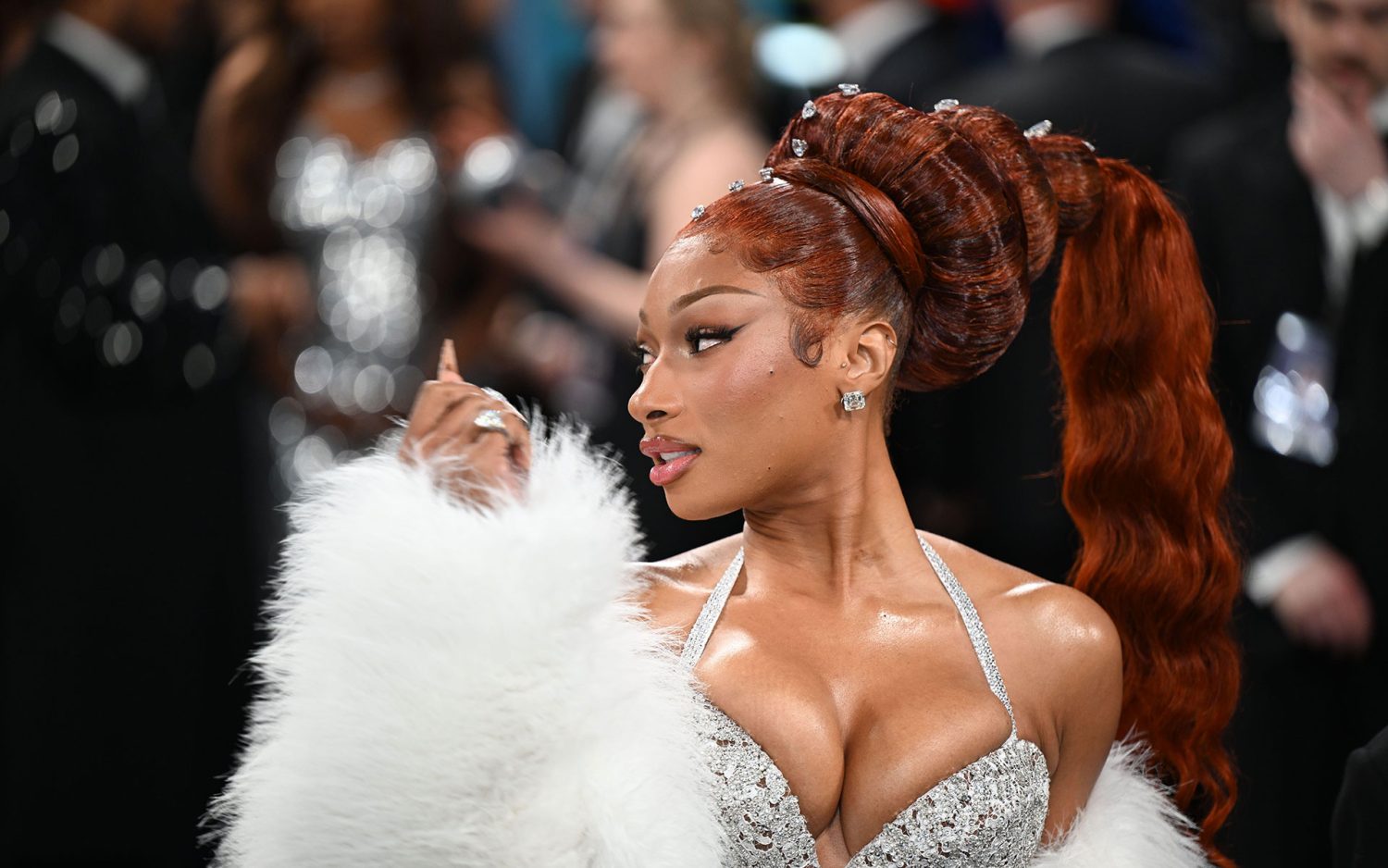 Person in glamorous dress with a high ponytail and white fur coat at a formal event, surrounded by other attendees.