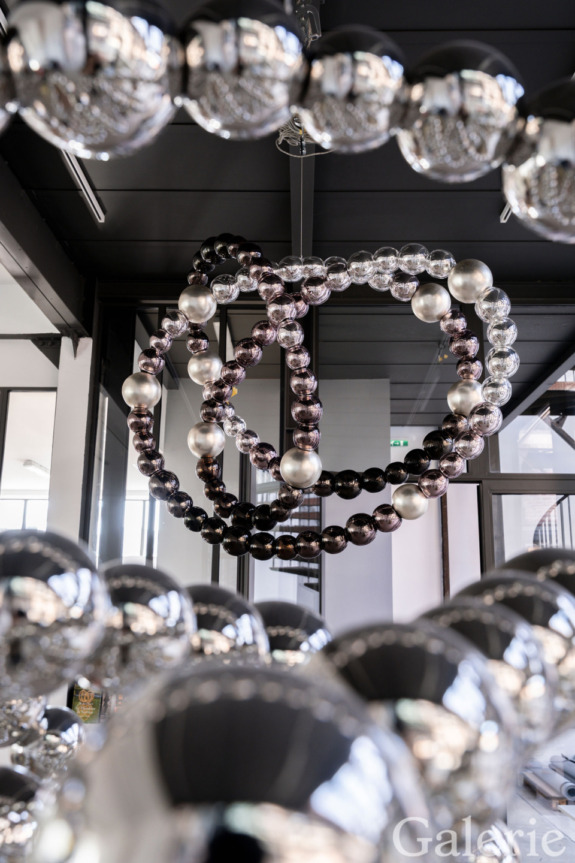 Artistic sphere sculpture with metallic finish, arranged in overlapping rings, displayed in a modern indoor gallery setting.