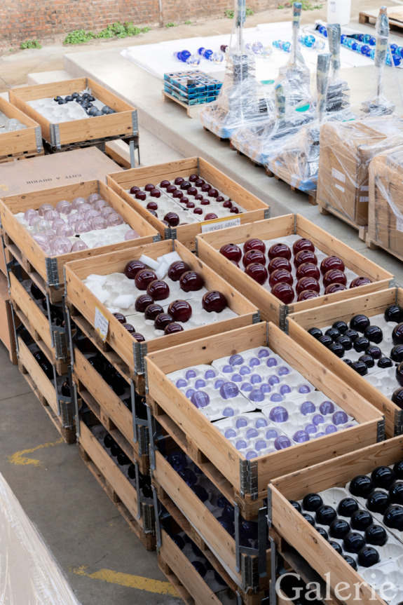 Wooden crates filled with various colored glass baubles stacked in a warehouse environment.