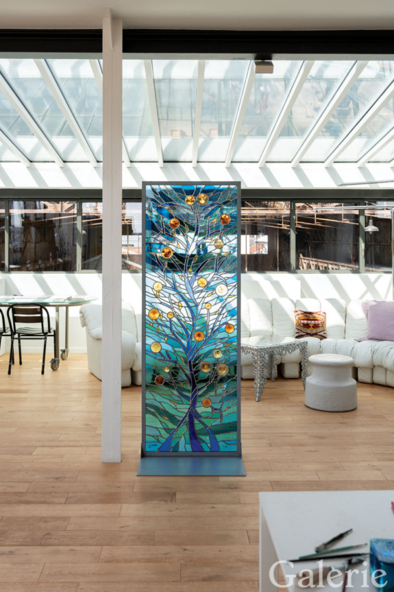 Stained glass panel with colorful tree design in modern living room with skylights and white furniture.