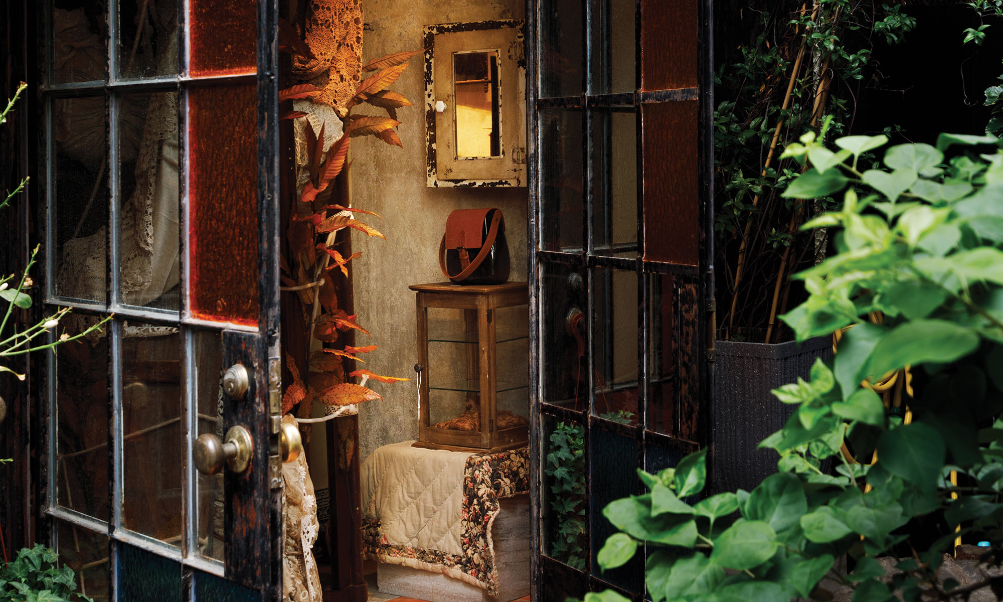 Cozy room with vintage mirror, plants, and a small wooden cabinet visible through an open glass door.