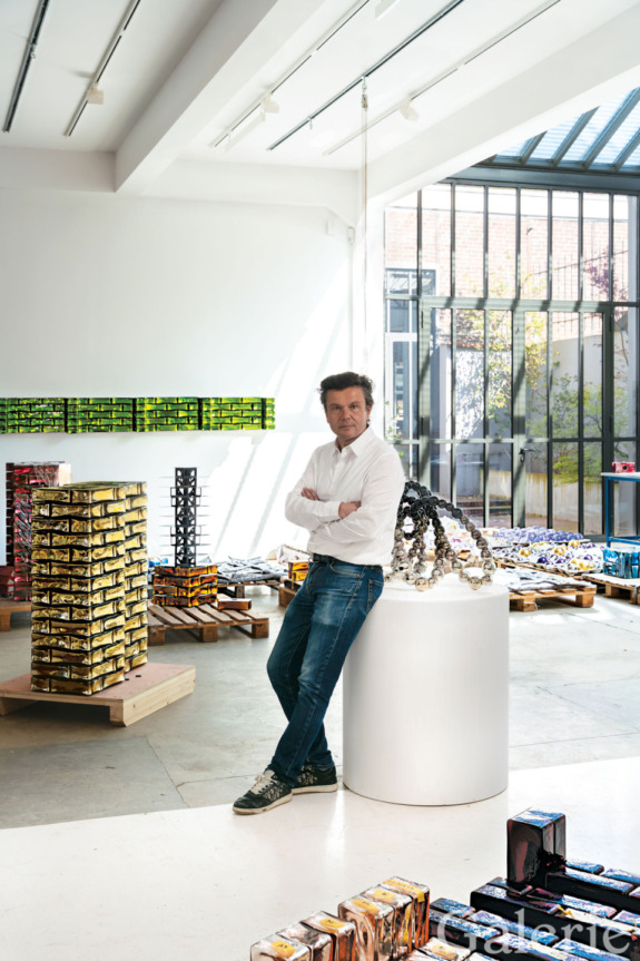 Person standing in a modern art studio surrounded by colorful sculptures and artworks, wearing casual jeans and a white shirt.
