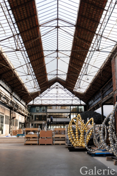 Spacious industrial warehouse with high glass ceilings and large, intricate metal sculptures placed on the floor.