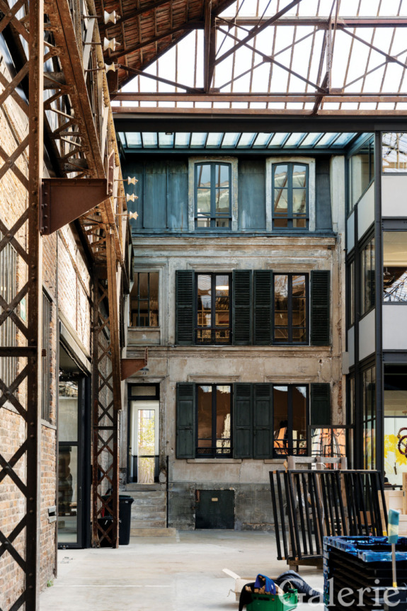 Industrial-style interior courtyard with metal beams, glass roof, and rustic building facade, featuring a blend of modern and vintage elements.