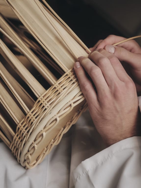 Hands weaving a basket with natural fibers, showcasing traditional craftsmanship and detailed handiwork.
