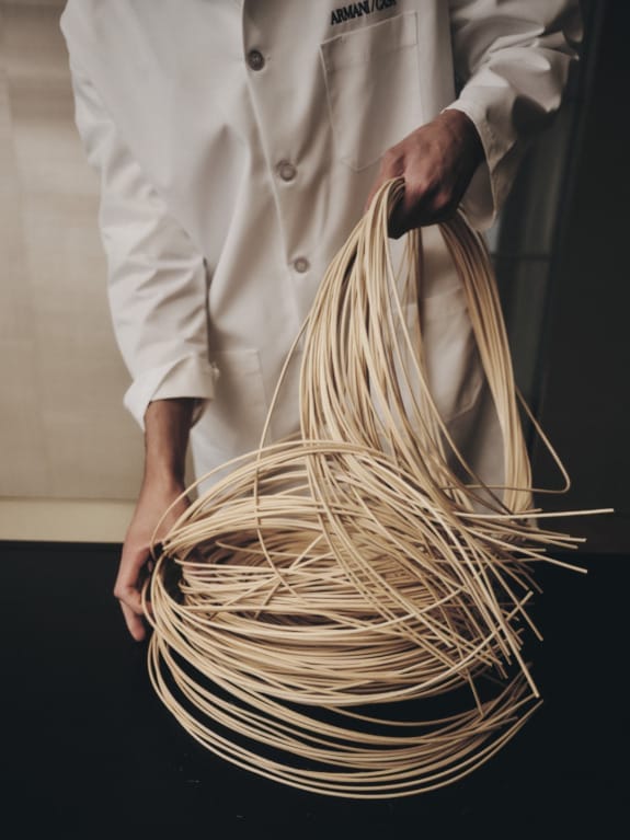 Chef in a white coat expertly handles bundles of raw spaghetti, preparing it on a black countertop.