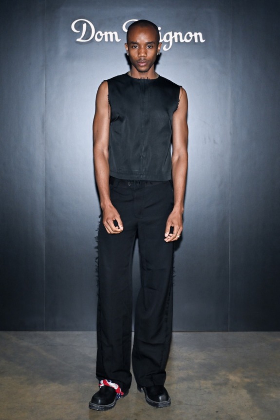 Person standing in front of a Dom Pérignon backdrop wearing a sleeveless black outfit and black shoes.