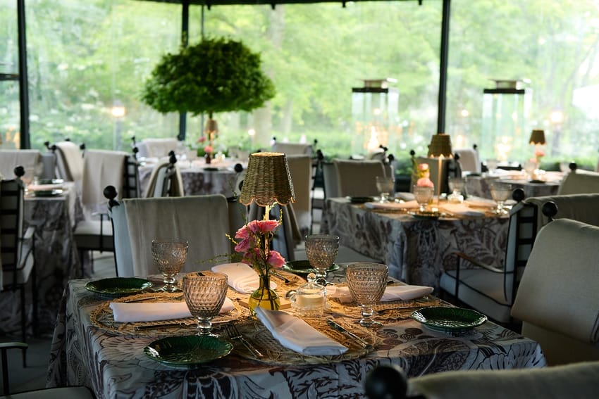 Elegant outdoor restaurant setup with neatly arranged tables, crystal glassware, floral centerpieces, and soft ambient lighting.