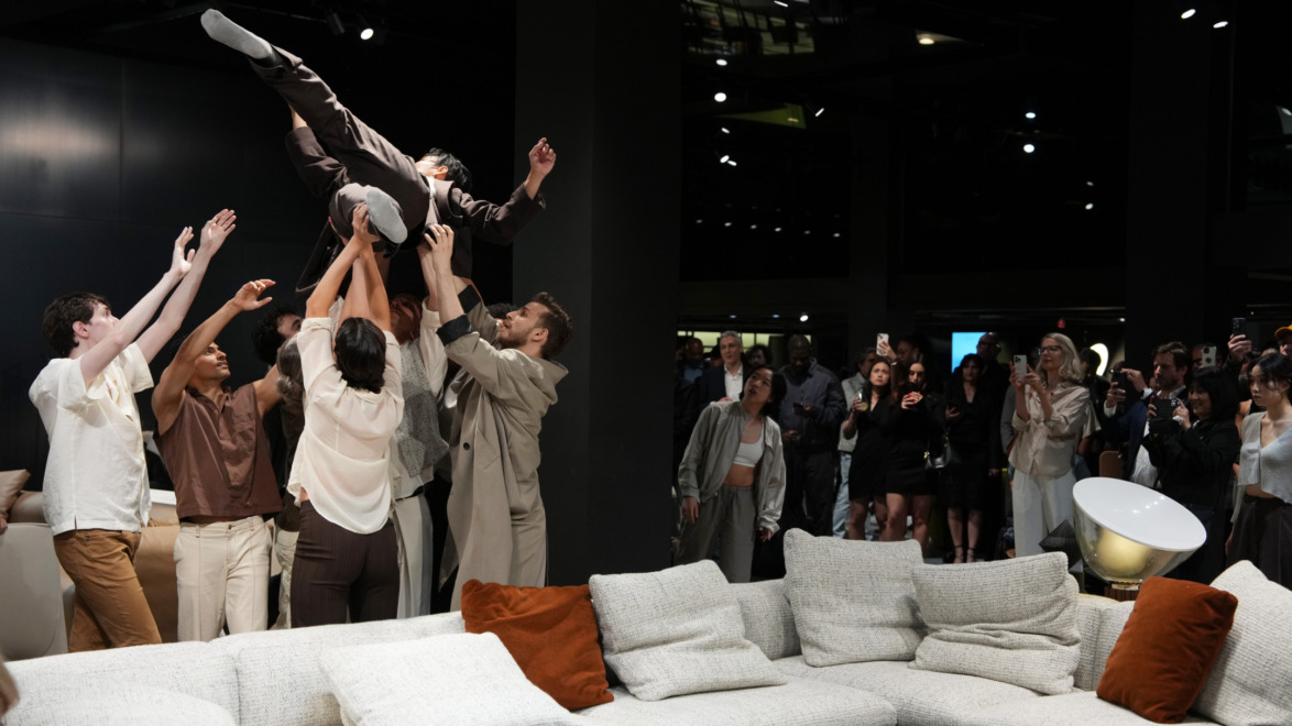 Group of people at an indoor event lifting a person above them, with a sofa and an audience in the background.