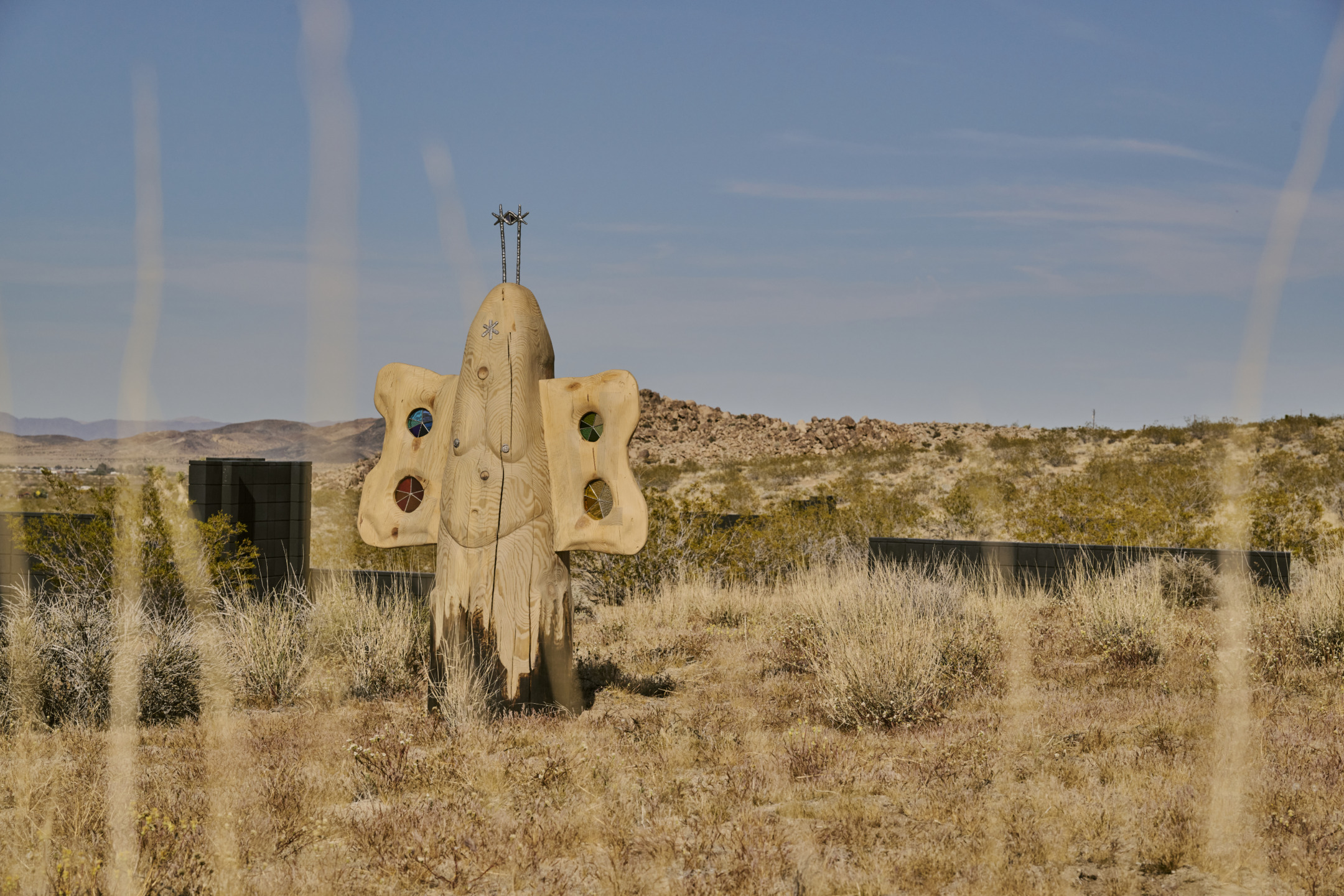 Sculpture resembling an abstract spaceship in a desert landscape with dry grass and distant hills under a clear blue sky