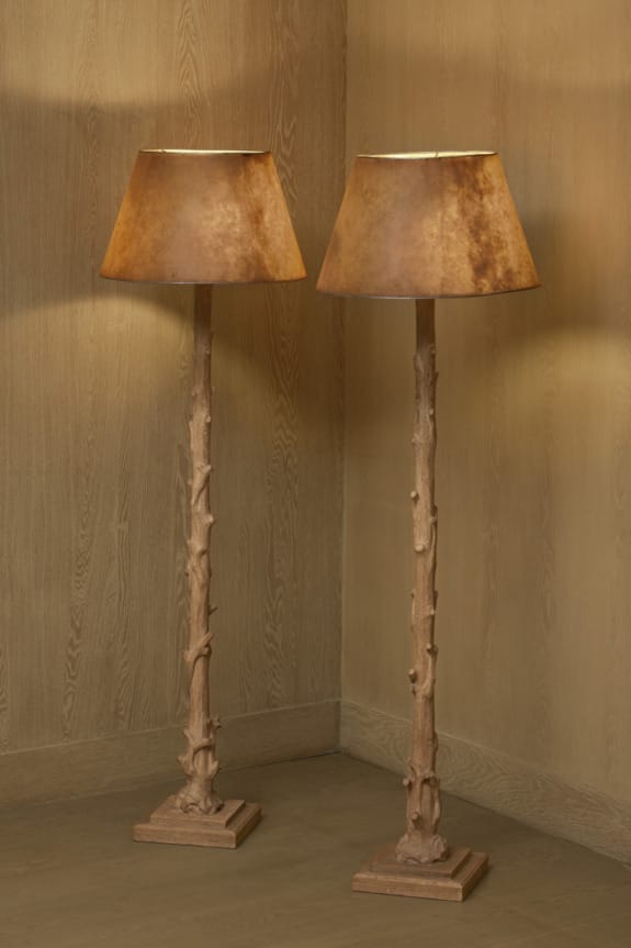 Two rustic floor lamps with branch-like wooden bases and warm brown lampshades in a cozy corner against wooden walls.