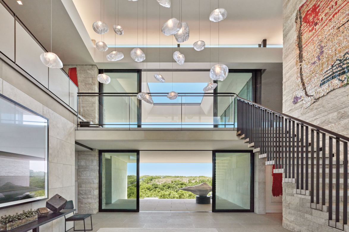 Modern open-concept interior with glass balcony, artistic ceiling lights, and large windows offering a scenic outdoor view.