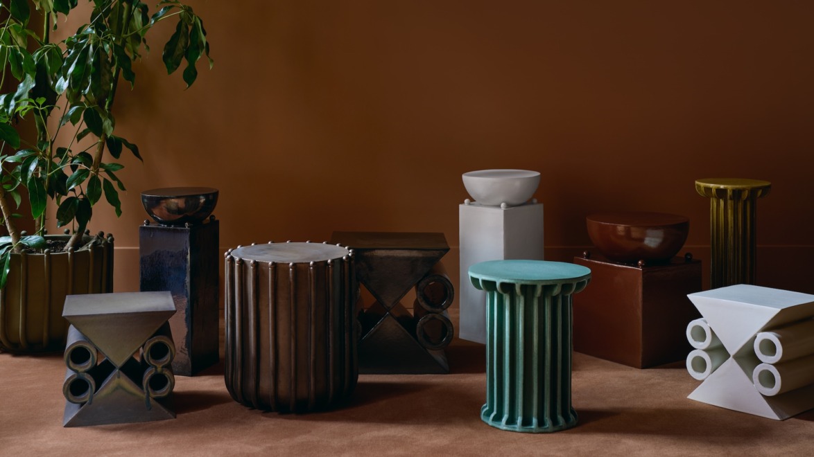 Assorted modern ceramic stools on a brown carpet with a green plant in the corner against a warm brown wall.