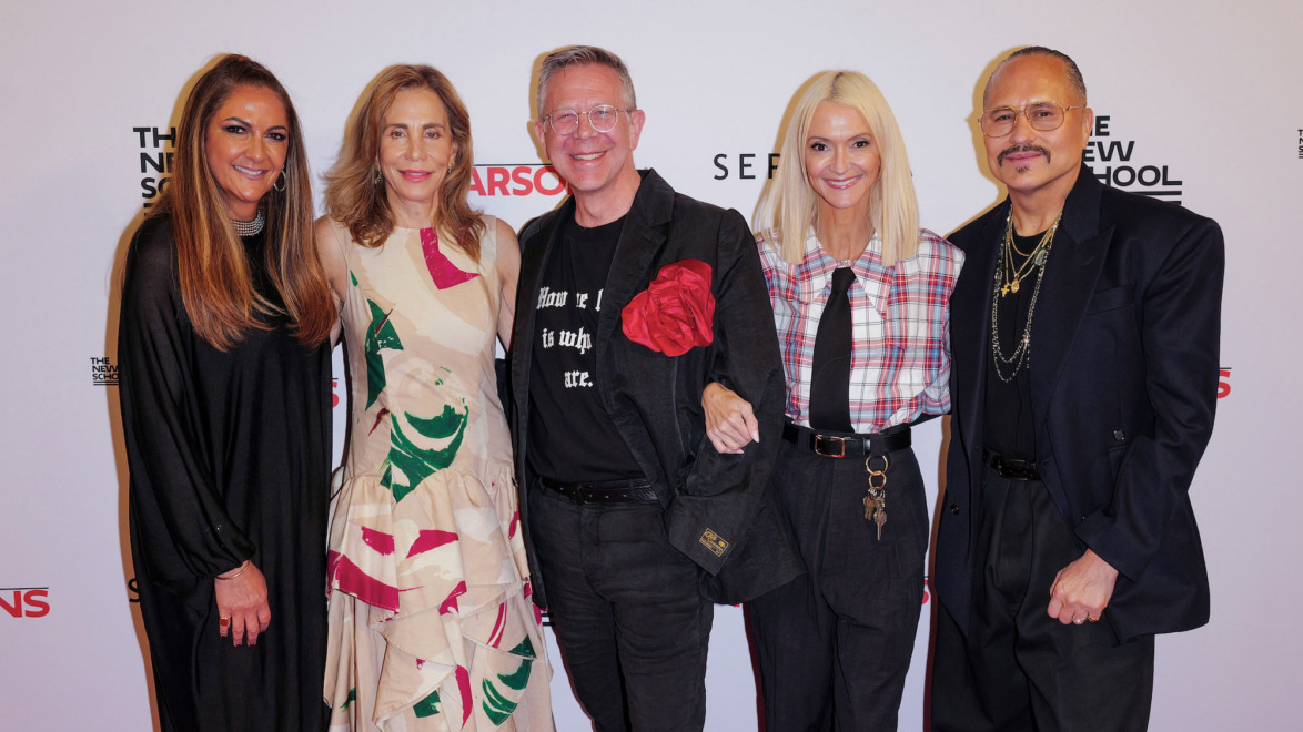 Group of five people smiling and posing together at an event, wearing fashionable attire.