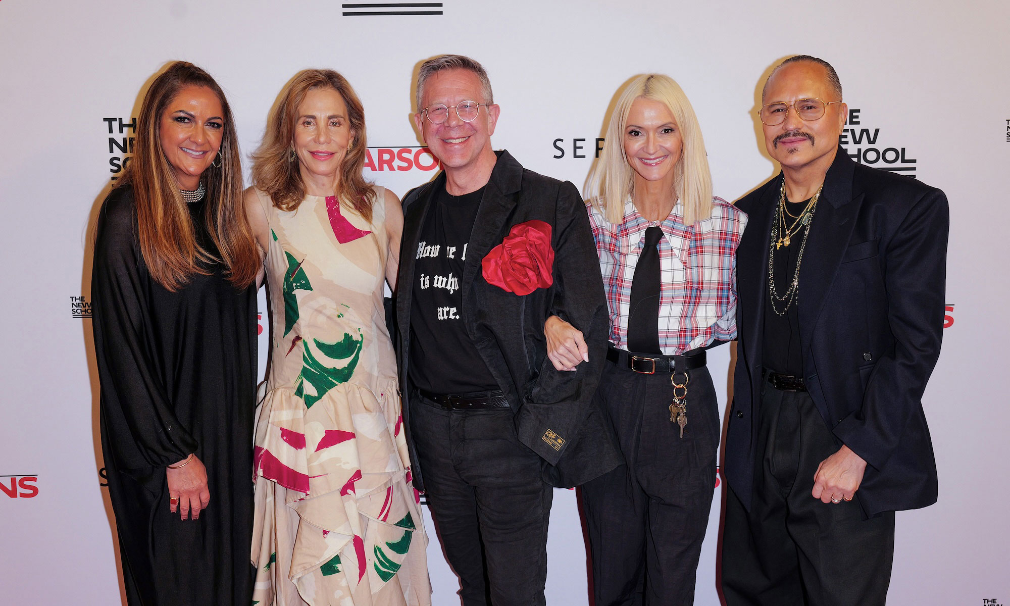 Group of five people smiling and posing together at an event, wearing fashionable attire.