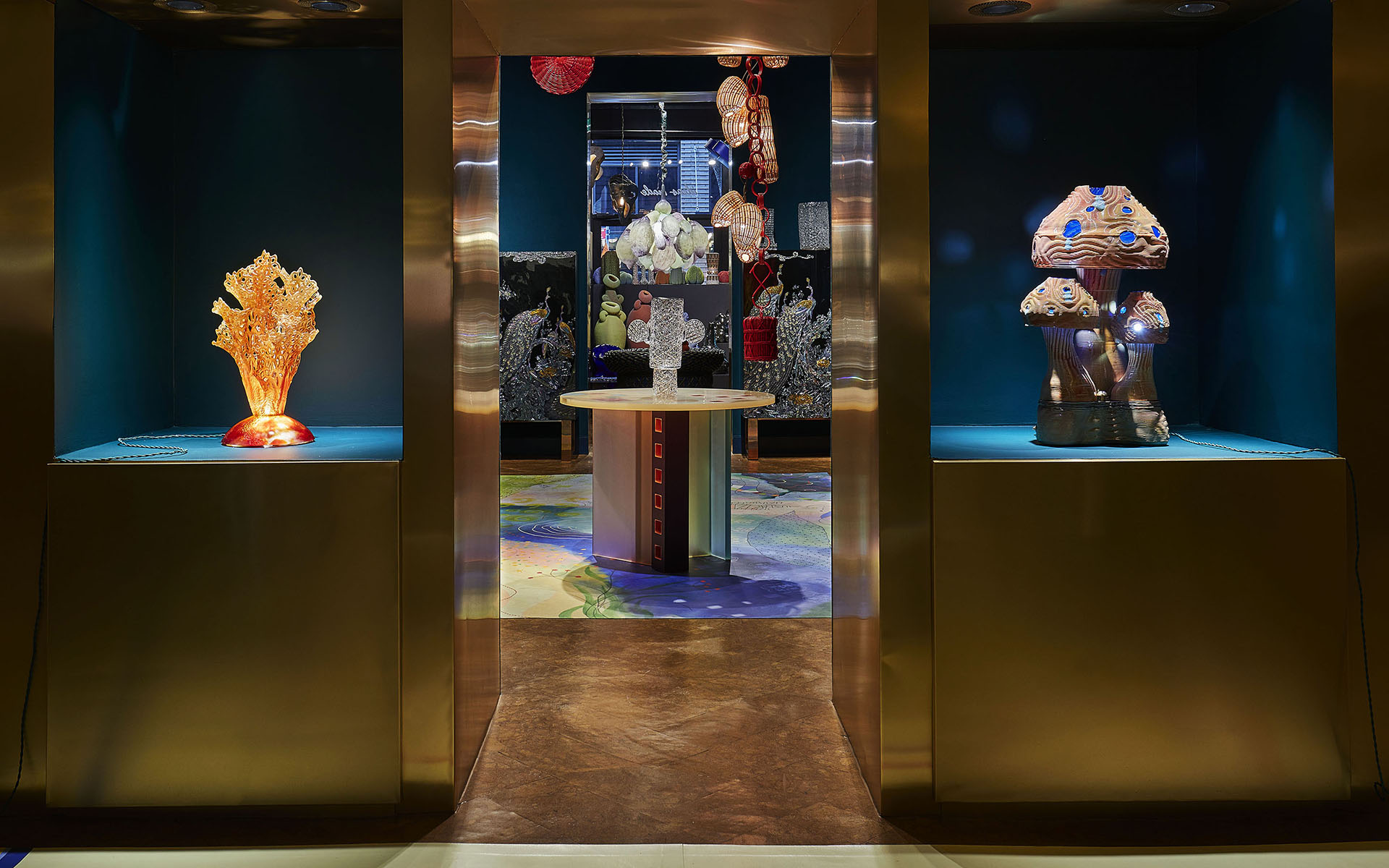 Art exhibit with colorful glass sculptures and intricate designs displayed in a dimly lit room with a central table.
