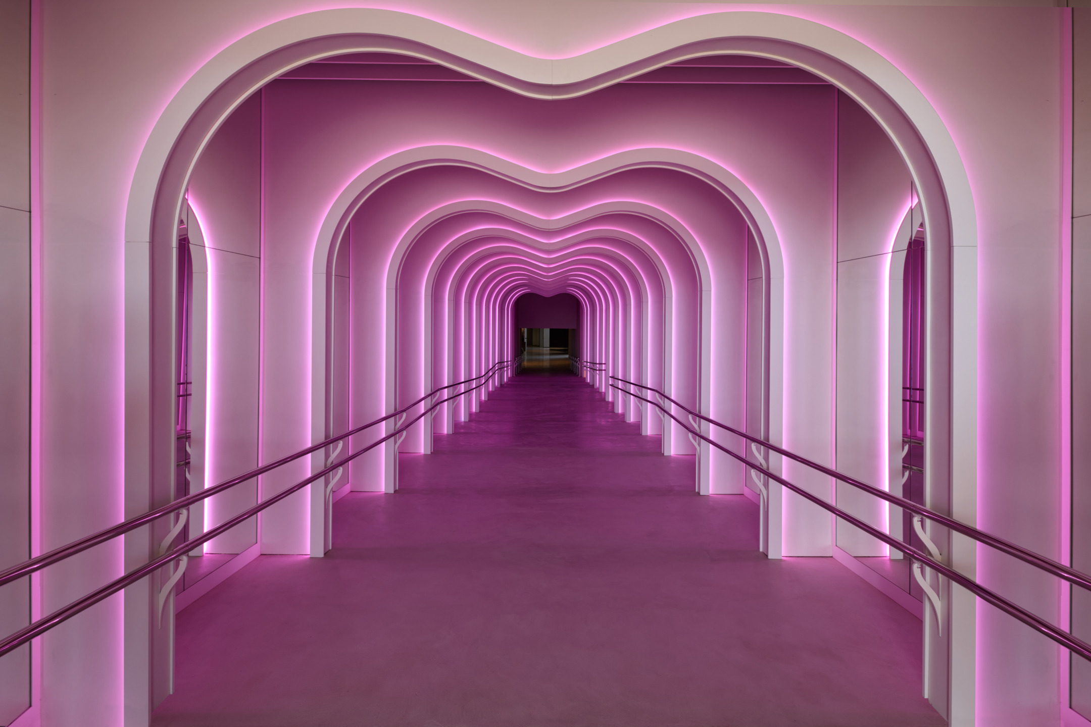 Futuristic corridor with arched, pink neon-lit walls and railings, creating a tunnel effect.