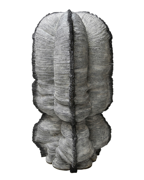 Abstract sculpture with layered, textured gray and black material forming a complex, vertical cylindrical shape.