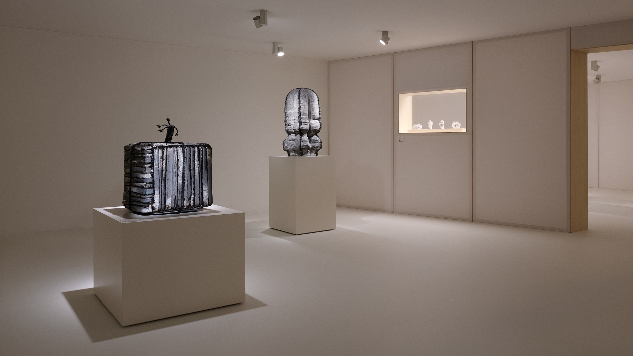 Minimalistic art gallery interior with sculptures on white pedestals, soft lighting highlighting the artwork in a serene environment.