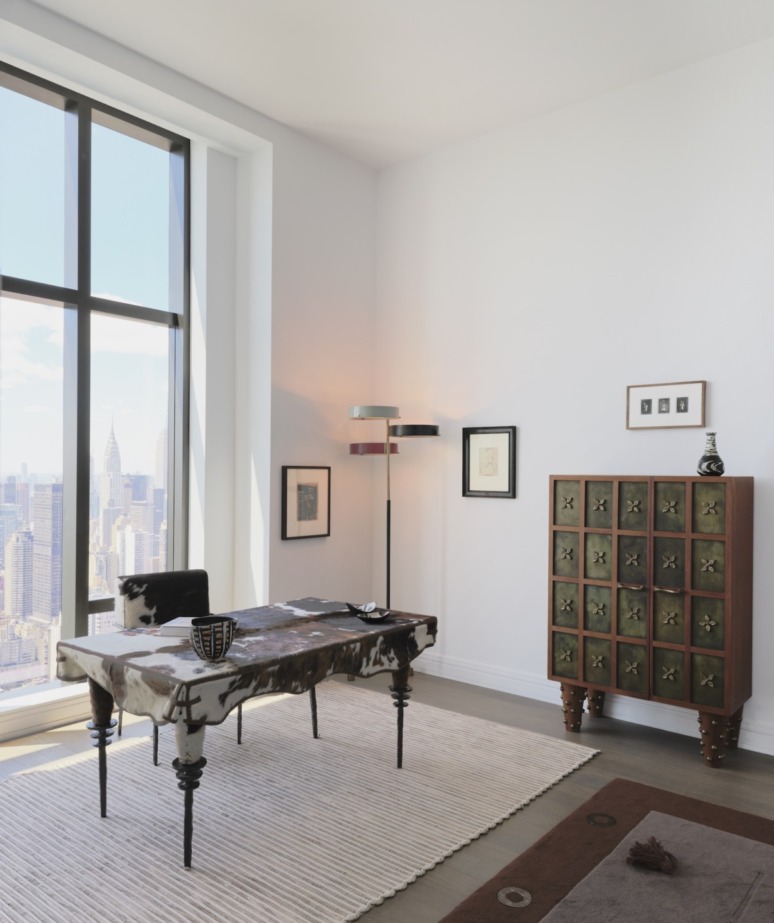 Modern office with a unique desk, floor lamp, and a tall cabinet, featuring large windows with a city view.