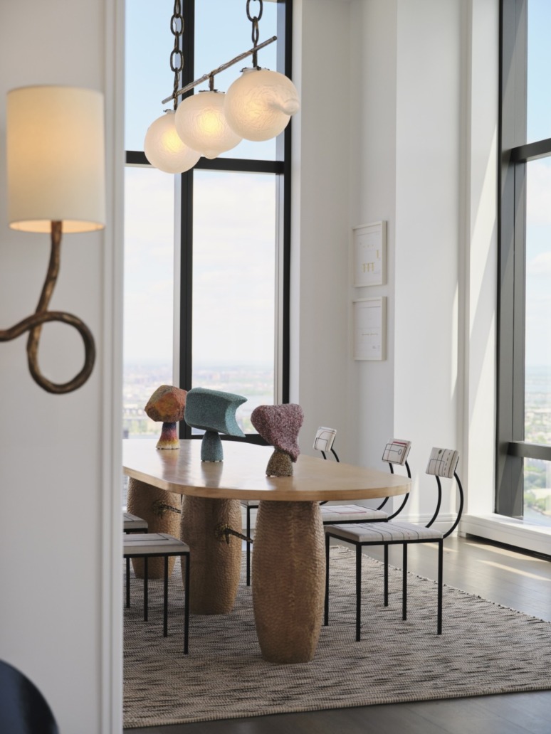 Modern dining area with large windows, wooden table, artistic decor, and metal chairs on a patterned rug.