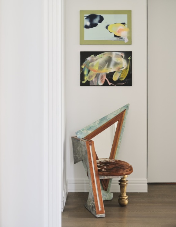 Artistic chair with colorful abstract paintings on a white wall in a modern interior setting.