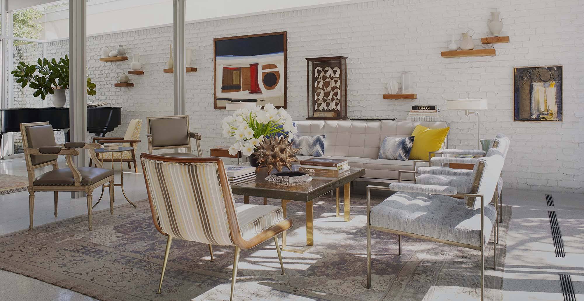 Modern living room with white brick wall, stylish furniture, colorful artwork, and decorative plants.